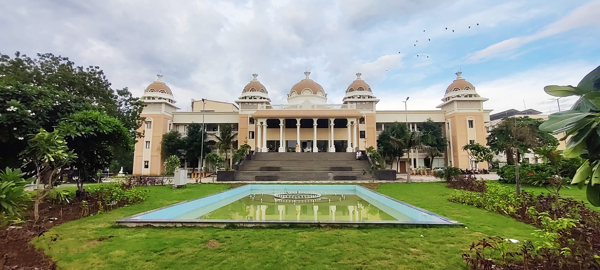 Large domed building, reflecting pool, green grounds, and birds in the sky.