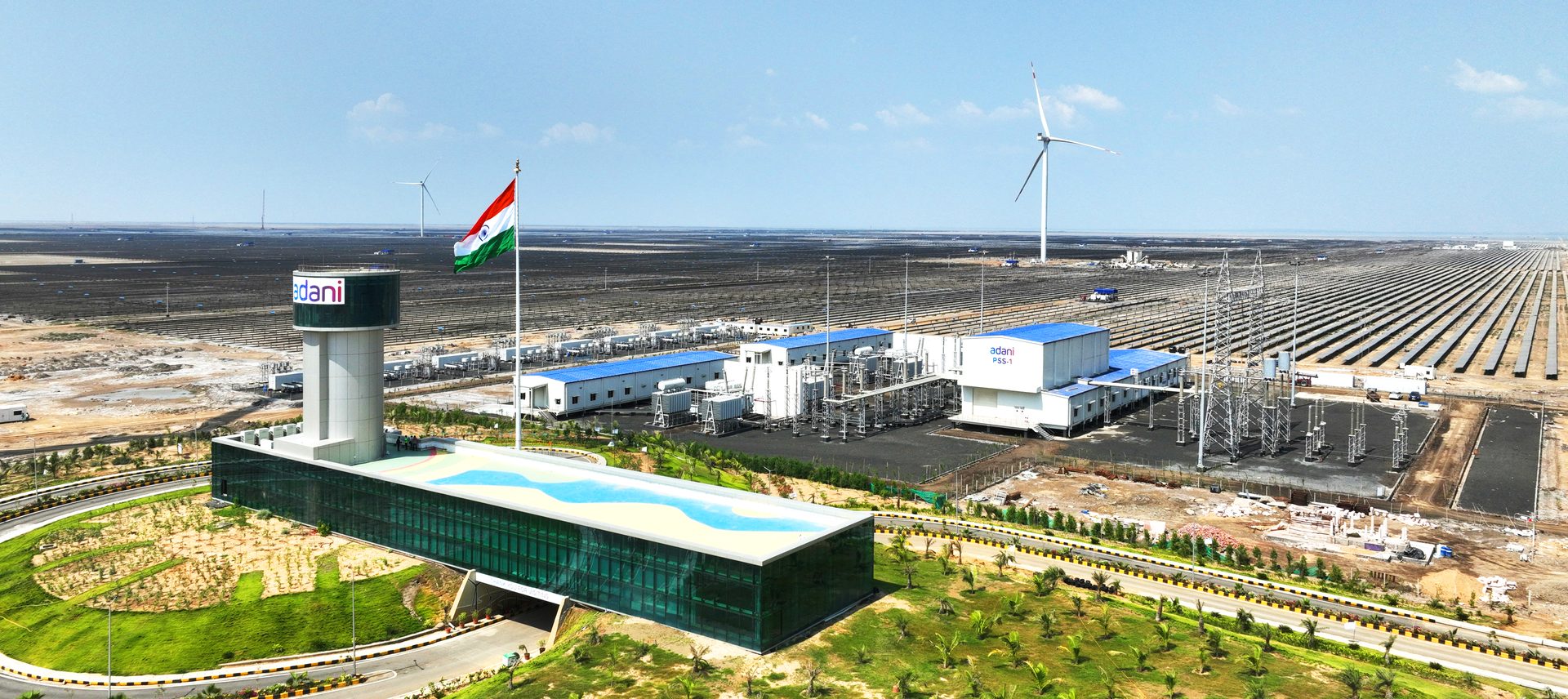 Aerial view of Adani's vast solar and wind power plant in India, with panels, turbines, and buildings.