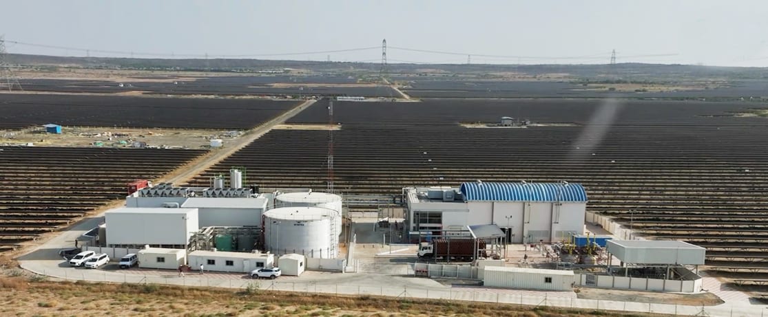 Vast solar farm with central buildings and rows of panels extending to the horizon.