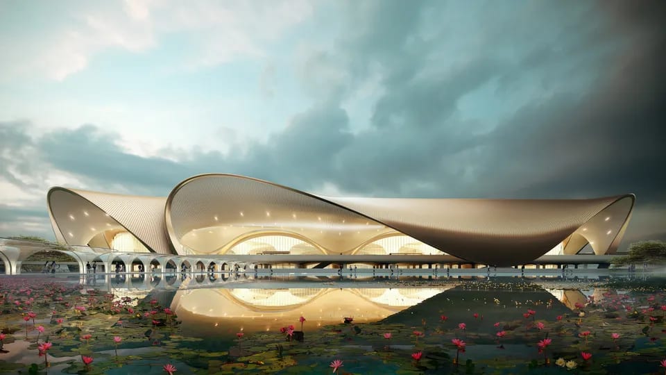 Curved modern building reflected in a lotus pond under a cloudy sky.