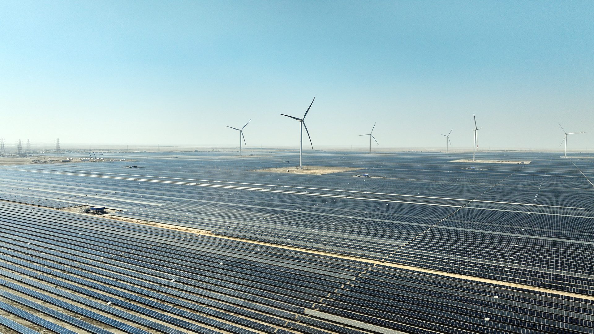 Vast solar farm and wind turbines under a clear sky.