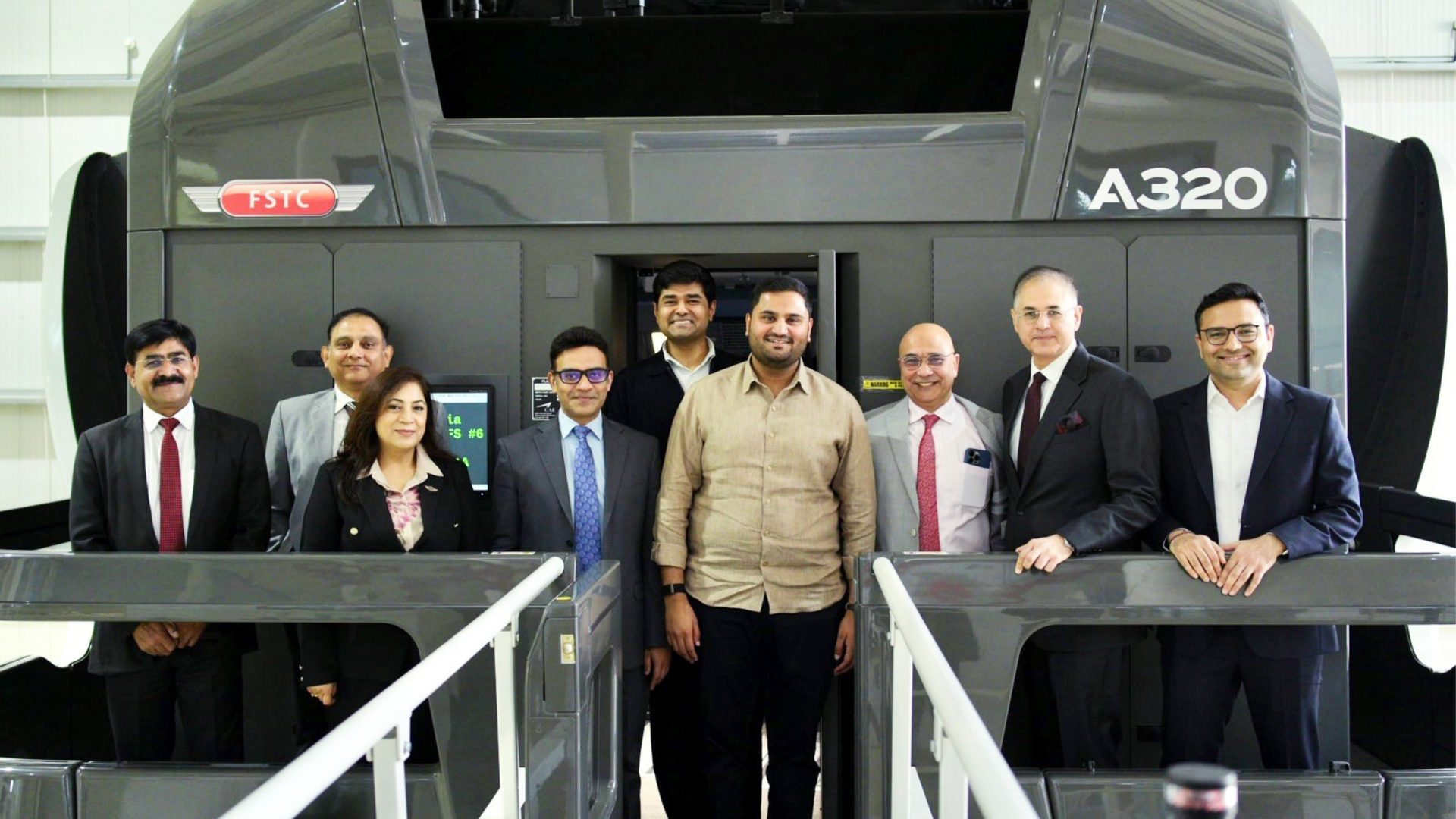Nine people smiling in front of an FSTC A320 flight simulator.