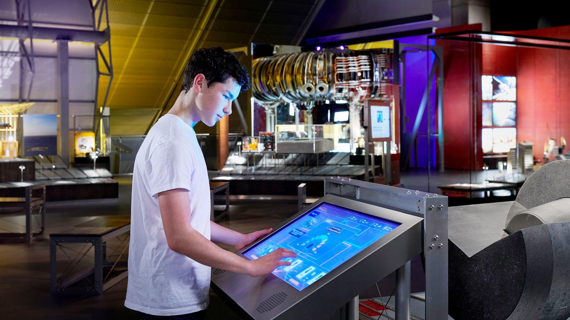 Teenager interacts with a large touchscreen in a museum exhibit showing a jet engine.