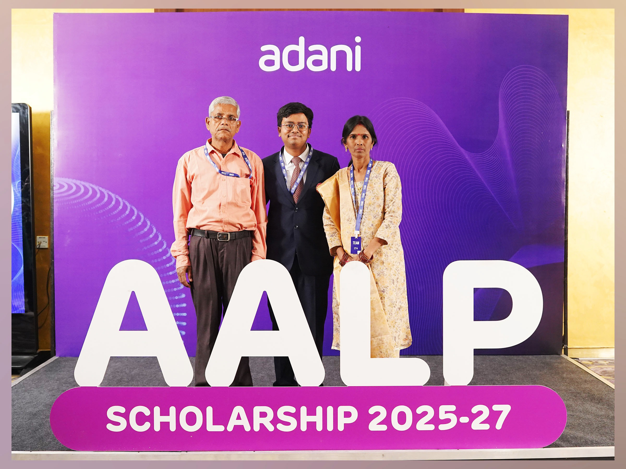 Three individuals stand in front of a purple Adani AALP Scholarship 2025-27 banner.