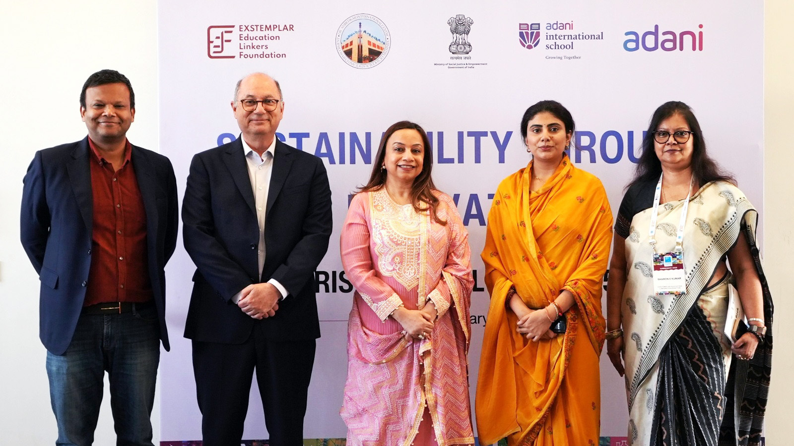 Five individuals (3 women, 2 men) standing at a "Sustainability" event with sponsor banners.