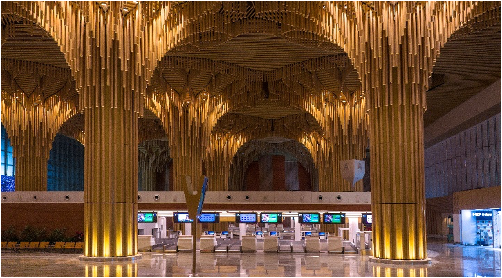 Modern airport interior with unique tree-like golden columns and ceiling, above empty check-in counters.