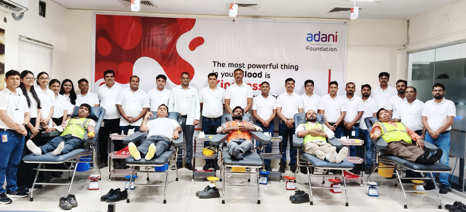 Adani Foundation staff and blood donors gather for a blood donation drive, under a banner.