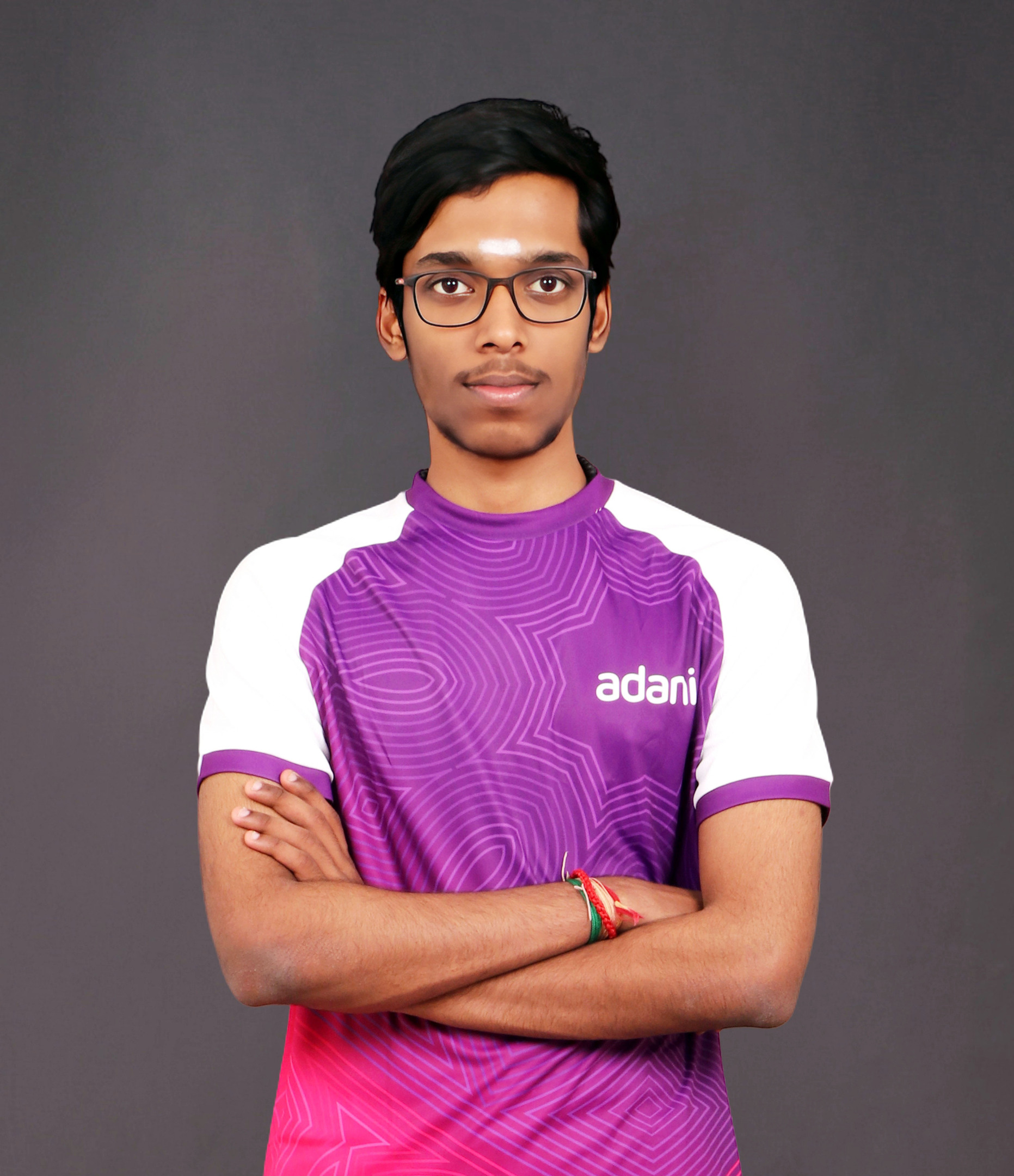 Young man in glasses and a purple and white Adani jersey, with arms crossed, looking at the camera.
