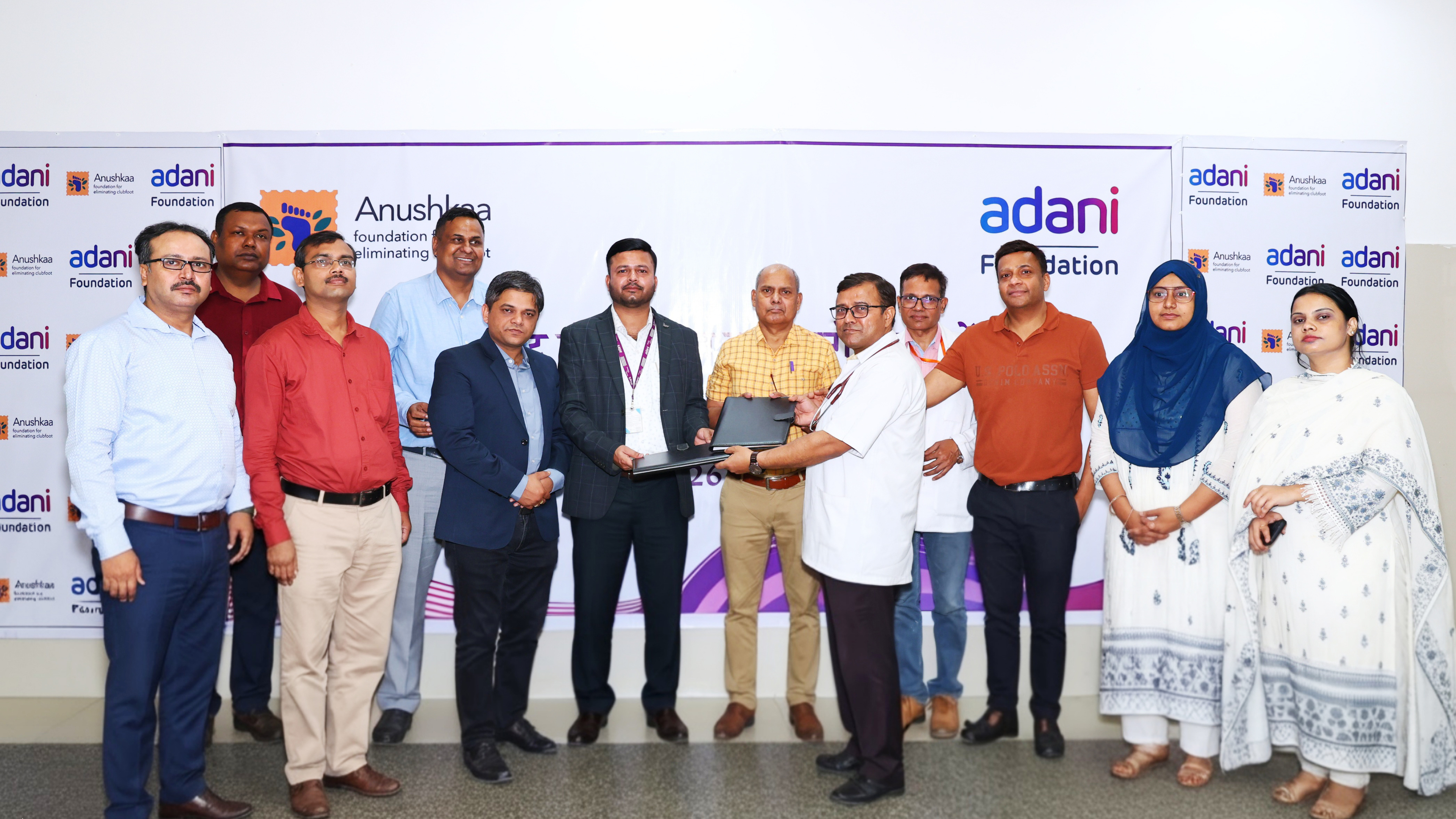 Adani and Anushka Foundations professionals gather for a group photo, with two men exchanging a laptop.