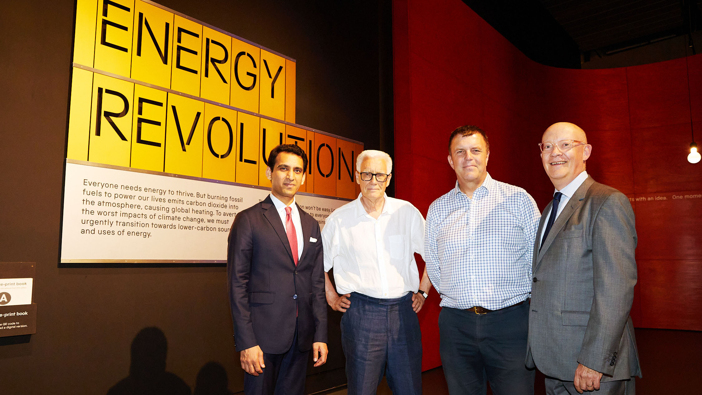 Four men stand before an "ENERGY REVOLUTION" exhibit, promoting energy transition.
