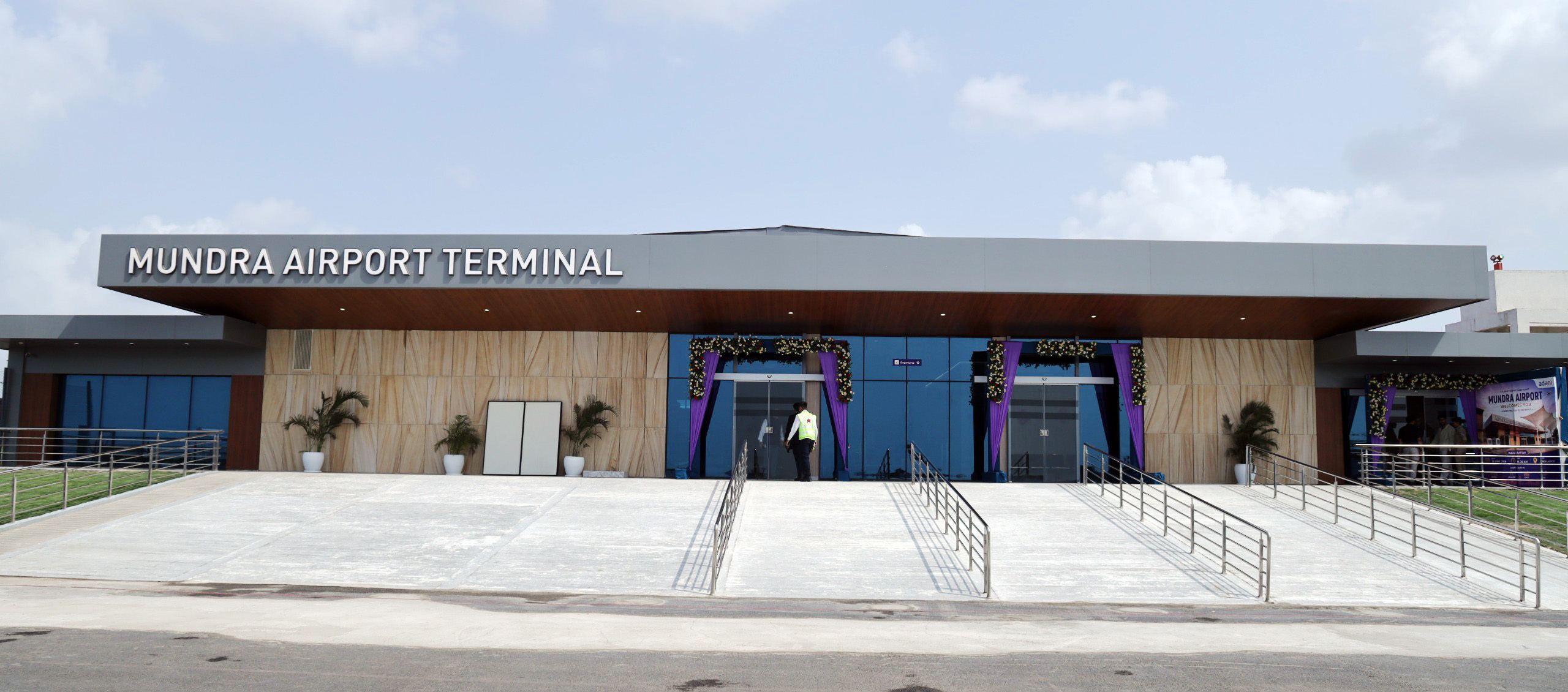 Exterior view of Mundra Airport Terminal entrance with ramps, glass doors, and purple decorations.