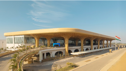 Modern airport terminal with a golden, tree-like column facade under a clear sky, an Indian flag nearby.