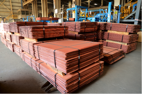 Stacks of reddish copper cathode plates, bundled and on pallets, in an industrial warehouse.
