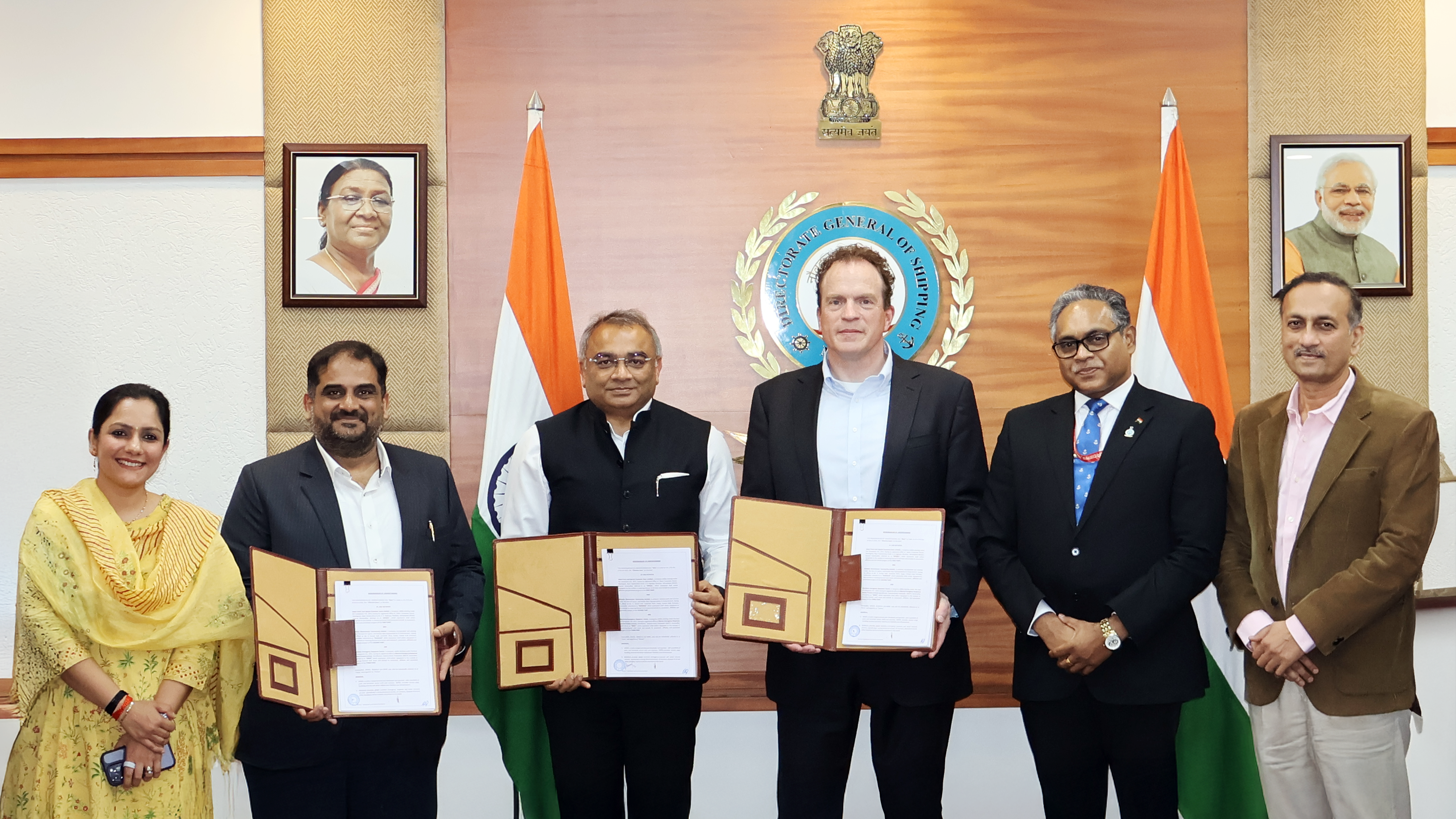 Six individuals, including a woman and five men, posing with documents and Indian flags for a photo.