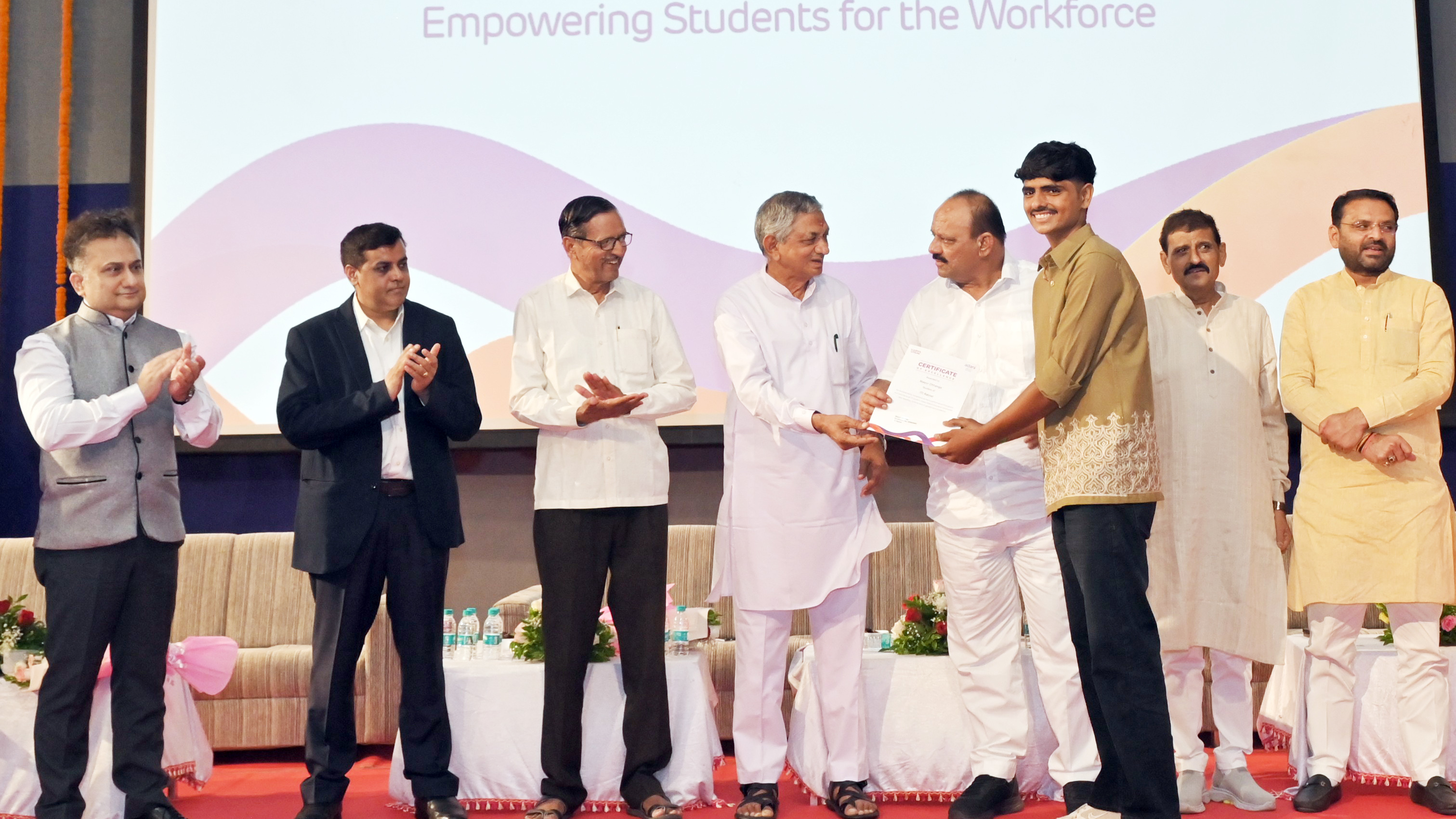 A group of officials and a student on stage during a certificate presentation ceremony.